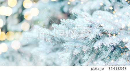 Blue branches of Christmas tree are decorated with garland against the background of falling snow 85418343