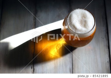 午後の強い光に照らされる丸みを帯びた背の低いグラスに注がれた泡立つビール 85421895