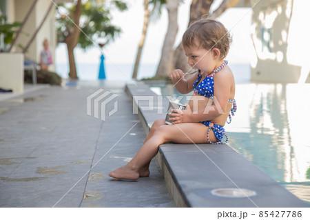little girl eating ice cream yogurt with spoon sitting by outdoor pool little girl eating ice cream yogurt with spoon sitting by outdoor pool 85427786