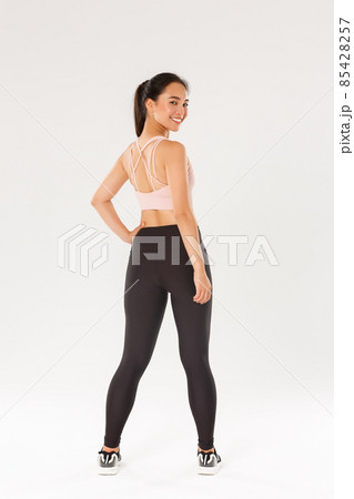 Full length of smiling slim and strong female fitness coach, female athelte in sportswear turn behind to look at camera with pleased, motivated expression, girl ready for workout, white background Full length of smiling slim and strong female fitness coach, female athelte in sportswear turn behind to look at camera with pleased, motivated expression, girl ready for workout, white background 85428257