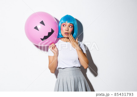 Cute and silly asian girl in blue wig, celebrating halloween, looking surprised at balloon with scary face 85431793