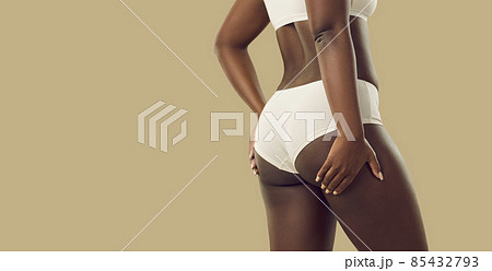 Attractive plus size black woman in underwear. Hot brown skinned model  wearing comfy natural cotton undies holding hands on thighs standing on  color background. Female body concept, rear back view Stock Photo