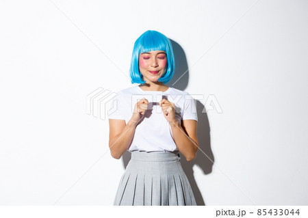 Portrait of beautiful asian girl in blue wig and halloween costume, daydreaming about shopping while holding credit card and smiling with closed eyes, standing over white background Portrait of beautiful asian girl in blue wig and halloween costume, daydreaming about shopping while holding credit card and smiling with closed eyes, standing over white background 85433044