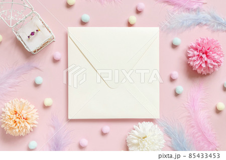 Square envelope between pastel flowers, pom-poms and feathers near ring in a gift box on pink Square envelope between pastel flowers, pom-poms and feathers near ring in a gift box on pink 85433453