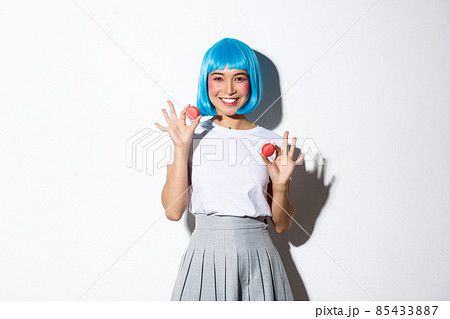Portrait of kawaii asian girl with glamour makeup, wearing blue wig, showing macaroons and smiling, standing over white background 85433887