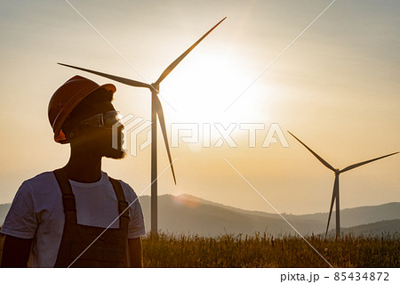 Engineer standing on field with windmills during sunset Engineer standing on field with windmills during sunset 85434872