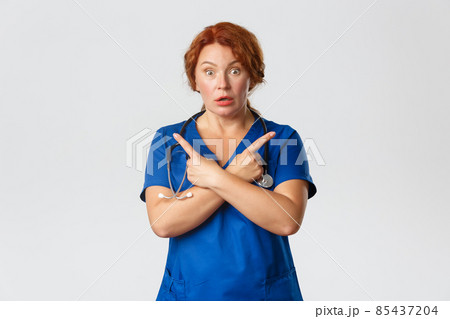 Medicine, healthcare and coronavirus concept. Confused and startled middle-aged redhead female doctor pointing sideways, left and right choices, asking question, look indecisive, grey background Medicine, healthcare and coronavirus concept. Confused and startled middle-aged redhead female doctor pointing sideways, left and right choices, asking question, look indecisive, grey background 85437204