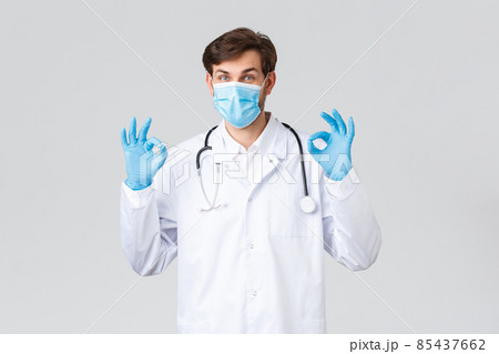 Hospital, healthcare workers, covid-19 treatment concept. Take it easy, all good. Doctor in medical mask, white scrubs and gloves, showing okay sign, approve and recommend medical treatment 85437662