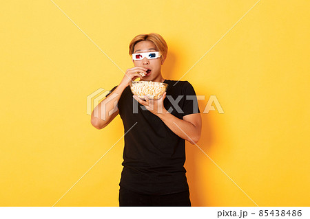 Impressed and thrilled asian guy attend cinema, watching movie or tv series in 3d glasses, eating popcorn and looking shocked, standing yellow background Impressed and thrilled asian guy attend cinema, watching movie or tv series in 3d glasses, eating popcorn and looking shocked, standing yellow background 85438486