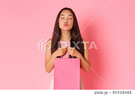 Beauty, fashion and lifestyle concept. Portrait of glamour flirty asian girlfriend holding shopping bag with clothes boyfriend bought, leaning for kiss and close eyes sensual, pink background Beauty, fashion and lifestyle concept. Portrait of glamour flirty asian girlfriend holding shopping bag with clothes boyfriend bought, leaning for kiss and close eyes sensual, pink background 85438488