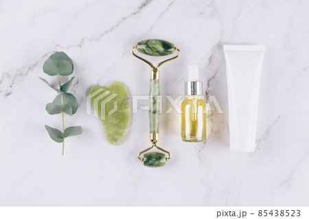 Flat lay with jade facial roller and gua sha tool with beauty serum, face oil and face moisturizer on white marble table background. Facial massage kit for lifting massage therapy, home spa. Mock up Flat lay with jade facial roller and gua sha tool with beauty serum, face oil and face moisturizer on white marble table background. Facial massage kit for lifting massage therapy, home spa. Mock up 85438523