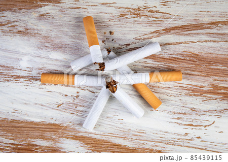 Stack of broken cigarettes on a white painted wooden background Stack of broken cigarettes on a white painted wooden background 85439115