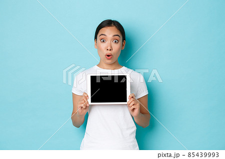 Portrait of excited and amazed asian girl gasping amazed and wondered, demonstrate awesome online store, showing digital tablet screen and looking at camera, standing light blue background Portrait of excited and amazed asian girl gasping amazed and wondered, demonstrate awesome online store, showing digital tablet screen and looking at camera, standing light blue background 85439993