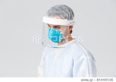 Covid-19, pandemic, healthcare workers fighting virus outbreak. Profile of tired young doctor in personal protective equipment, PPE suit and medical mask, looking at patient with coronavirus symptoms Covid-19, pandemic, healthcare workers fighting virus outbreak. Profile of tired young doctor in personal protective equipment, PPE suit and medical mask, looking at patient with coronavirus symptoms 85440536
