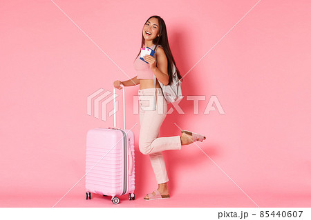 Travelling, holidays and vacation concept. Full-length of carefree asian girl, exchange student or tourist with backpack and suitcase, smiling broadly and holding passport with flight tickets 85440607