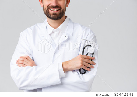 Hospital, healthcare workers, covid-19 treatment concept. Cropped shot of bearded smiling doctor in white scrubs, cross arms like professional physician or therapist, holding stethoscope 85442141