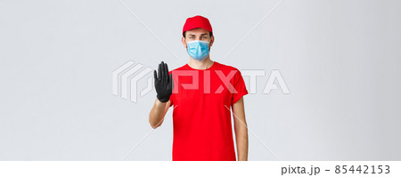 Covid-19, self-quarantine, online shopping concept. Confident delivery man in red uniform, gloves and face mask, raise hand in stop sign, prevent client step to storage without protective equipment Covid-19, self-quarantine, online shopping concept. Confident delivery man in red uniform, gloves and face mask, raise hand in stop sign, prevent client step to storage without protective equipment 85442153