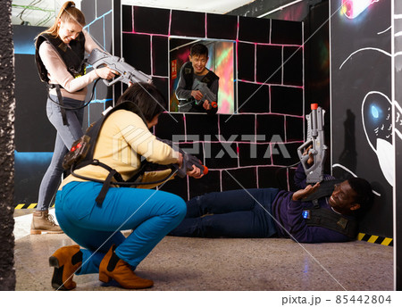 Modern people of different nationalities with laser pistols playing laser tag on dark labyrinth Modern people of different nationalities with laser pistols playing laser tag on dark labyrinth 85442804