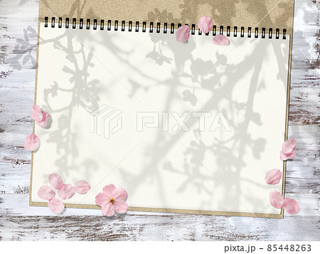 桜の影が写るウッドデッキとスケッチブックに、桜の花が散る背景 85448263