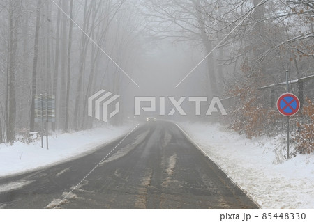 Bad weather driving - foggy hazy country road. Motorway - road traffic. Winter time and snow. Bad weather driving - foggy hazy country road. Motorway - road traffic. Winter time and snow. 85448330