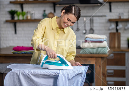 Girl smoothing out wrinkles on the shirt with a steam iron 85458973