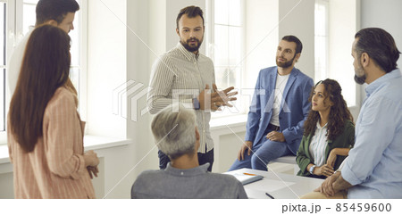 Group of people having a work meeting. Serious young male team leader, corporate manager, businessman or business coach standing in office and talking to group of employees. Website banner background 85459600
