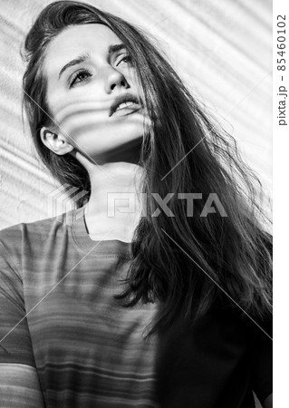 Pensive dreamy woman with pleasant appearance wearing T-shirt standing, cute girl looking away. Black and white photography, indoor studio shot illuminated by sunlight from window. Pensive dreamy woman with pleasant appearance wearing T-shirt standing, cute girl looking away. Black and white photography, indoor studio shot illuminated by sunlight from window. 85460102