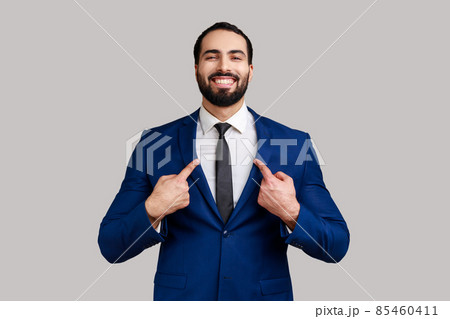 Portrait of bearded man with toothy smile on face pointing fingers on himself, confident positive businessman, wearing official style suit. Indoor studio shot isolated on gray background. 85460411