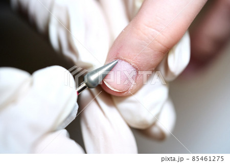 Woman in nail salon receiving manicure in beauty salon by beautician who use electric nail file drill with burst flying dust and debris around. Concept of nail care.  85461275