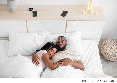 Calm millennial african american female and male sleeping at night, hugging on bed in bedroom interior Calm millennial african american female and male sleeping at night, hugging on bed in bedroom interior 85462330
