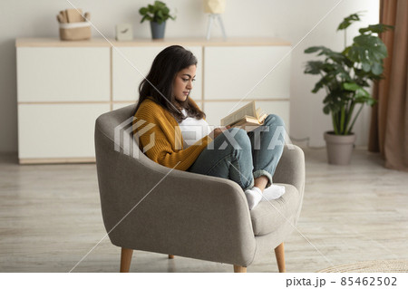 Focused arab lady sitting in armchair, reading book in living room, enjoying lazy morning with interesting story Focused arab lady sitting in armchair, reading book in living room, enjoying lazy morning with interesting story 85462502