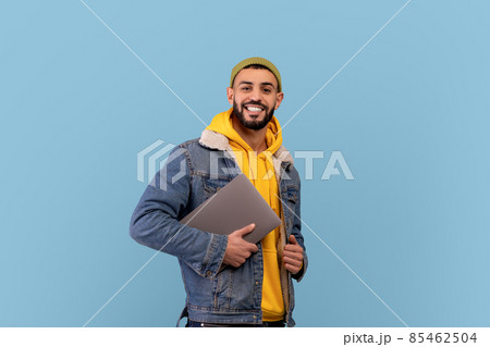 Happy middle eastern guy holding laptop and smiling at camera, arabic man with pc computer over blue background 85462504