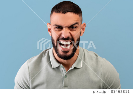 Portrait of furious arab man shouting with rage at camera, screaming with fury, standing over blue background Portrait of furious arab man shouting with rage at camera, screaming with fury, standing over blue background 85462811