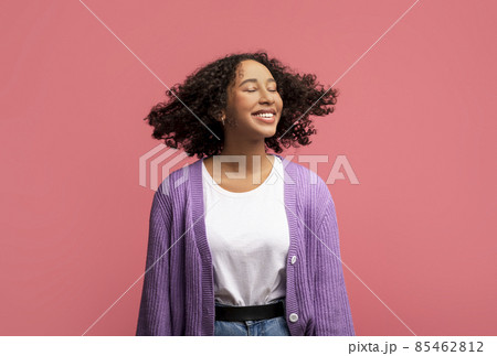 Portrait of smiling African American female model posing with healthy curly flying hair on pink studio background 85462812