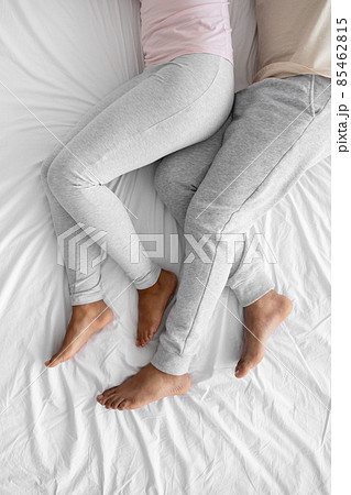 Cropped young african american husband and wife in domestic clothes lie on white bed, relaxing in free time Cropped young african american husband and wife in domestic clothes lie on white bed, relaxing in free time 85462815