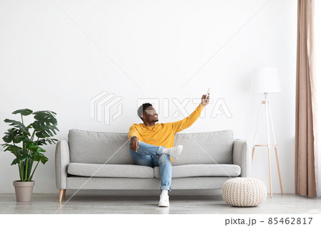 Relaxed african american guy sitting on couch, turning on AC Relaxed african american guy sitting on couch, turning on AC 85462817