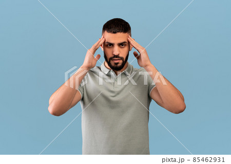 Middle eastern man suffering from headache, massaging temples to get rid of pain, standing over blue background 85462931