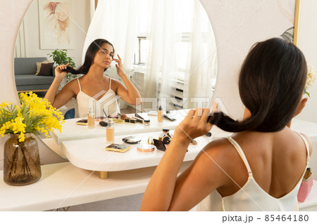 brunette woman with long straight dark hair and clean skin doing make up routine 85464180