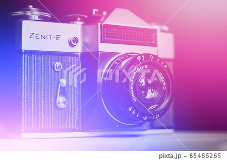 Berdsk, Russia - 3 jan 2022: Blurred Soviet old film camera Zenit-E with Industar 50-2 lens. Abstract background with color gradient. Trendy neon light. Purple, blue, pink, cyan 85466265