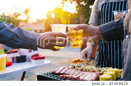 Friends and bbq party hold a plastic beer mug to celebrate the New Year holidays. Friends and bbq party hold a plastic beer mug to celebrate the New Year holidays. 85469819