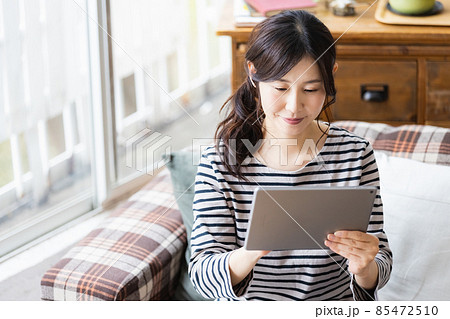 リビングルームでタブレットPCを見る女性 リビングルームでタブレットPCを見る女性 85472510