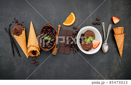 Chocolate ice cream flavours in bowl with dark chocolate and cacao nibs setup on dark stone background . Chocolate ice cream flavours in bowl with dark chocolate and cacao nibs setup on dark stone background . 85473013