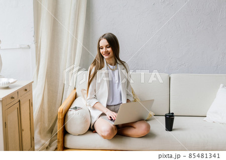 Beautiful young woman working on laptop computer while sitting at the living room, drinking coffee 85481341
