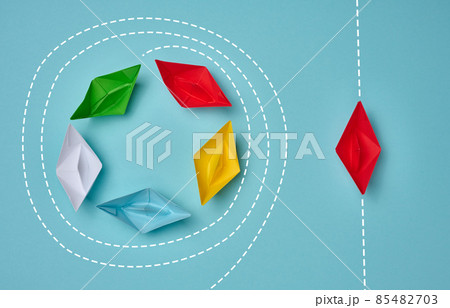 a group of paper boats floats in a circle, another red floats in a straight line. Strong leader concept, different vision, strong business. Looping over an idea 85482703