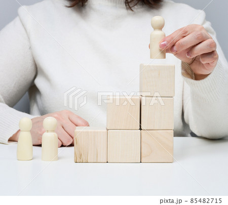 woman in a white sweater puts a wooden figurine on the podium. The concept of employee search, career advancement. Talented employee woman in a white sweater puts a wooden figurine on the podium. The concept of employee search, career advancement. Talented employee 85482715