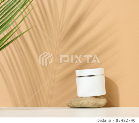 white round plastic jar for cosmetic products on a brown background. Palm leaf shadow. Blank for branding products, mock up 85482740