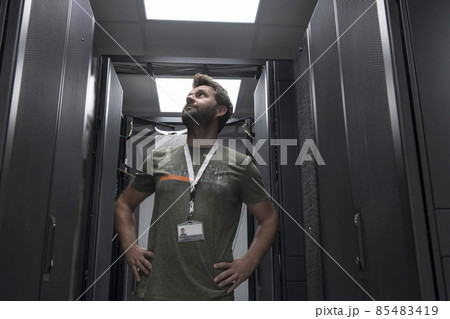 Portrait of male technician or network administrator standing brave as a hero with arms crossed in data center server room. 85483419