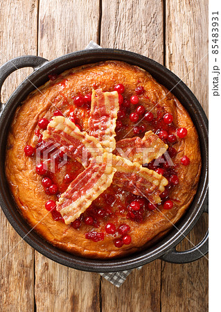 Traditional Swedish egg cake aggakaka which is served as a main course with fried bacon and lingonberries closeup in the pan. Vertical top view 85483931