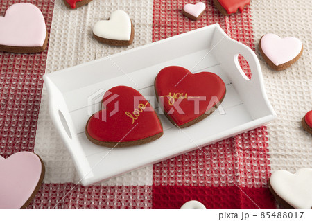 Two heart-shaped cookies with red sugar icing on wooden tray. Valentines Day, breakfast for loving Two heart-shaped cookies with red sugar icing on wooden tray. Valentines Day, breakfast for loving 85488017