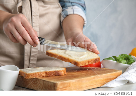 Woman spreading sauce on sandwich at light grey marble table, closeup 85488911